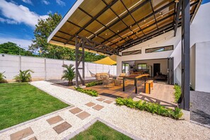 A modern outdoor patio area with a pergola, seating, and a view of the interior. - Stylish 'Casa Nonos' Home w/ Yard & Fire Pit! (Playas del Coco)