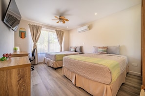 Ein Schlafzimmer mit zwei Betten, einem Schreibtisch, einem Stuhl, einem Deckenventilator und einer Klimaanlage.