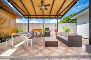 An outdoor patio with a ceiling fan, a barbecue grill, a dining table with benches, and a sofa. - Chic 'Alpinias' Condo w/ Pool Access, Near Beach (Playas del Coco)