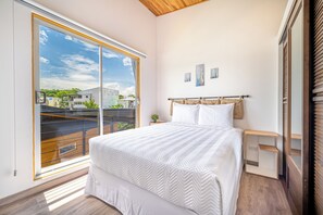 A bedroom with a large window, a bed with white bedding, a wooden headboard, and a small bedside table with a plant. - Chic 'Alpinias' Condo w/ Pool Access, Near Beach (Playas del Coco)