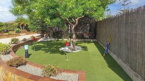 Jardí tancat amb gespa artificial, un arbre i una zona de jocs.