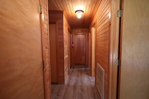 A wooden hallway with a ceiling light fixture, a door at the end, and a fire extinguisher mounted on the wall. - 4 Bedroom Oceanfront Home in Kitty Hawk, NC. JAX’S PLACE (Kitty Hawk)