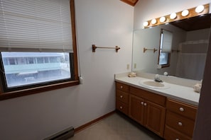 Een badkamer met raam, wastafel, spiegel en verlichting.