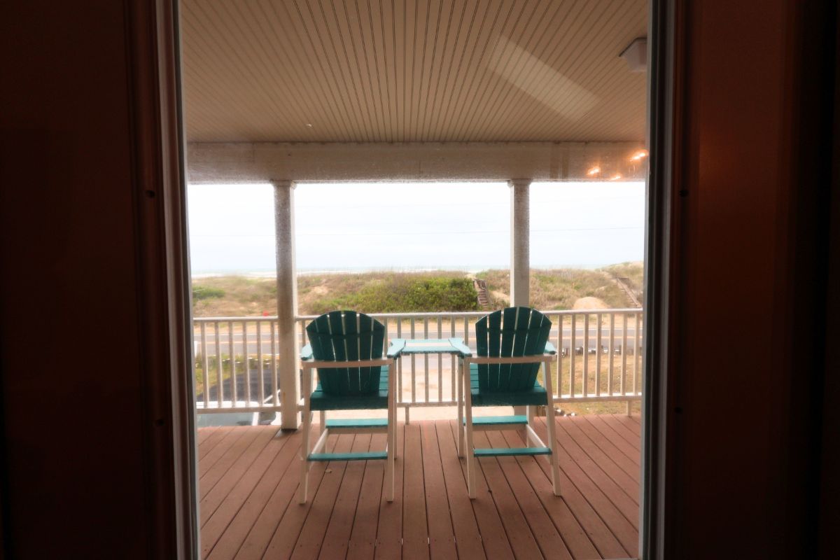 A wooden deck with two green chairs and a small table, overlooking a grassy landscape.