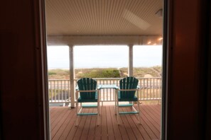 A wooden deck with two green chairs and a small table, overlooking a grassy landscape. - 4 Bedroom Oceanfront Home in Kitty Hawk, NC. JAX’S PLACE (Kitty Hawk)