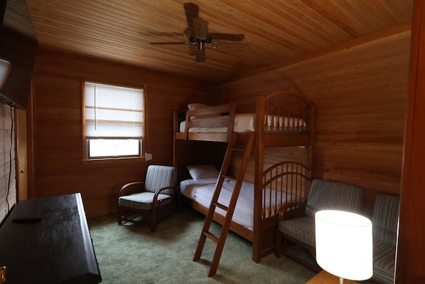 Een houten kamer met stapelbedden, een bureau, een stoel, een lamp en een plafondventilator.