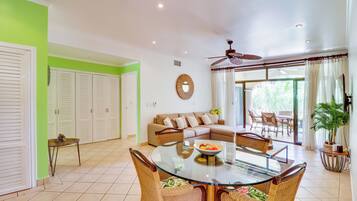 A living room with a glass-top dining table, wicker chairs, a sofa, and a ceiling fan.