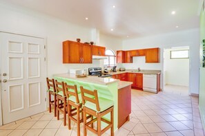 A kitchen with wooden cabinets, a dining area with chairs, and a tiled floor.