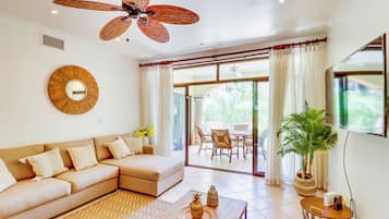 A spacious living area with a large sofa, a dining table, and a ceiling fan.