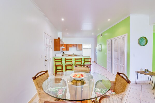 Una cocina moderna con armarios verdes, una zona de comedor con una mesa de vidrio y una pared de acento verde.