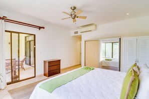 Un dormitorio con cama, cómoda, ventilador de techo, unidad de aire acondicionado y puerta corrediza de vidrio que da a un balcón.