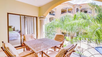Un balcon avec une table et des chaises, une vue sur un immeuble doté de balcons, et un jardin luxuriant et verdoyant.