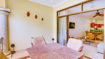 A room with a dining table, chairs, a ceiling fan, and a view into another room with a kitchen area.