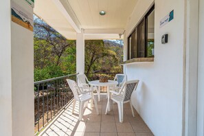 A balcony with a table and chairs, a view of trees, and a window with a sign. - Playas del Coco Condo w/ Pool: Walk to Beach! (Playas del Coco)