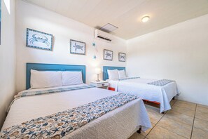 A hotel room with two beds, each with a blue headboard, white bedding, and a nautical-themed bedspread. There are wall-mounted air conditioning units and framed pictures of sea creatures on the walls. - Playas del Coco Condo w/ Pool: Walk to Beach! (Playas del Coco)