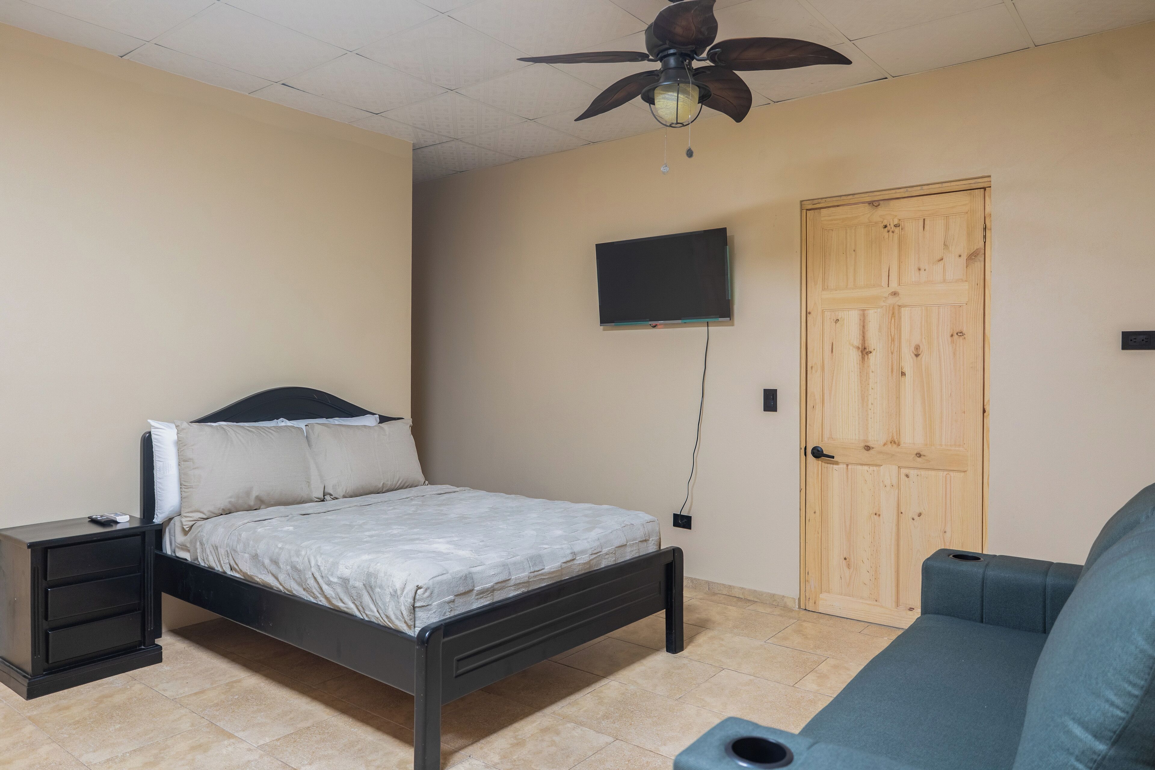 A bedroom with a bed, a nightstand, a television mounted on the wall, and a wooden door.