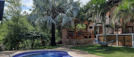 Ein Schwimmbecken mit einer gefliesten Kante, umgeben von üppiger Vegetation und einer Holzterrasse.