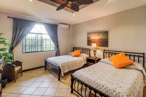 A bedroom with two beds, a ceiling fan, a window with curtains, a plant, and a painting on the wall. - Walk to Flamingo Beach: 2-Unit Base w/ Ocean Views (Flamingo Beach)
