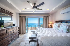 Een hotelkamer met een bed, een dressoir, een televisie, een plafondventilator en uitzicht op zee.