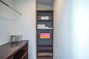 A narrow hallway with a wooden shelf unit against the wall, containing folded towels and a small, dark-colored pet bed. - Relaxing 3BR Ocean-View Condo | 2 Balconies (Playas del Coco)