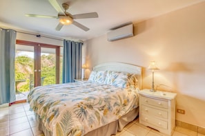Ein Schlafzimmer mit einem Bett, einem Nachttisch, einer Lampe, einem Deckenventilator und Blick auf Grünflächen außerhalb.