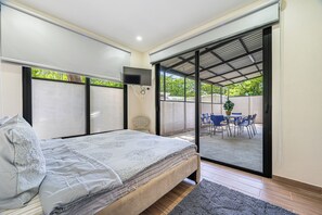 A bedroom with a bed, a TV, and a sliding glass door leading to an outdoor area with a table and chairs. - Modern Playas del Coco Home w/ Pool & Patio! (Playa Carrillo)