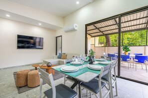 A modern dining area with a long table set for a meal, a sofa, and a TV mounted on the wall. - Modern Playas del Coco Home w/ Pool & Patio! (Playa Carrillo)