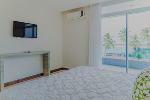 Hotelkamer met een bed, een flatscreen televisie aan de muur, een klein houten console tafeltje en een groot raam met uitzicht op palmbomen en een zwembad.
