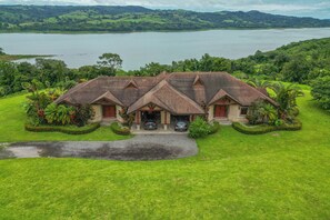 A large house with a spacious lawn, a driveway, and a car parked in front. - Stunning Lake Arenal Views: Duplex Unit w/ Patio! (La Fortuna)