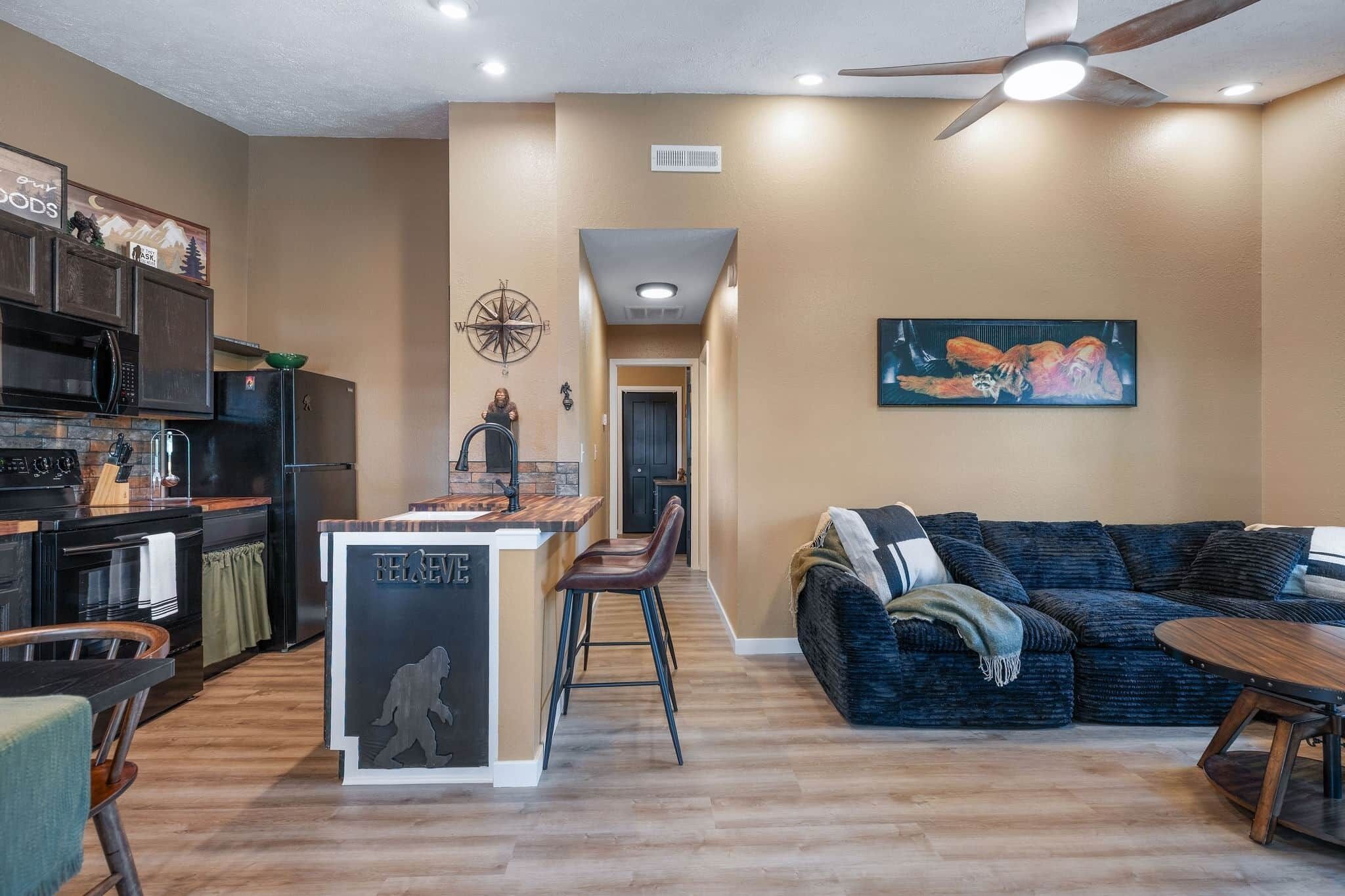 A modern kitchen with dark appliances, a central island, and a dining area with a dark blue sofa and a small round table.
