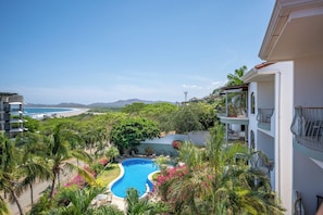 A residential area with a swimming pool surrounded by lush greenery and a view of the beach and ocean. - Walk to the Beach & Town! Tamarindo Condo (Tamarindo)