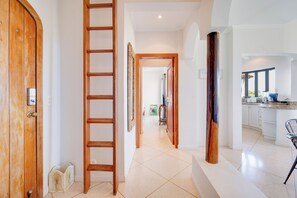 A hallway with a wooden door, a wooden ladder, and a kitchen area with a chair and counter. - Walk to the Beach & Town! Tamarindo Condo (Tamarindo)