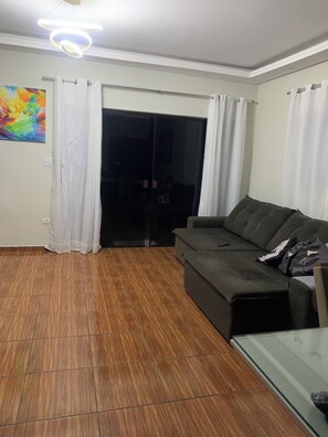 Ein Wohnzimmer mit einem dunkelgrauen Sofa, einem Glastisch und Holzboden.