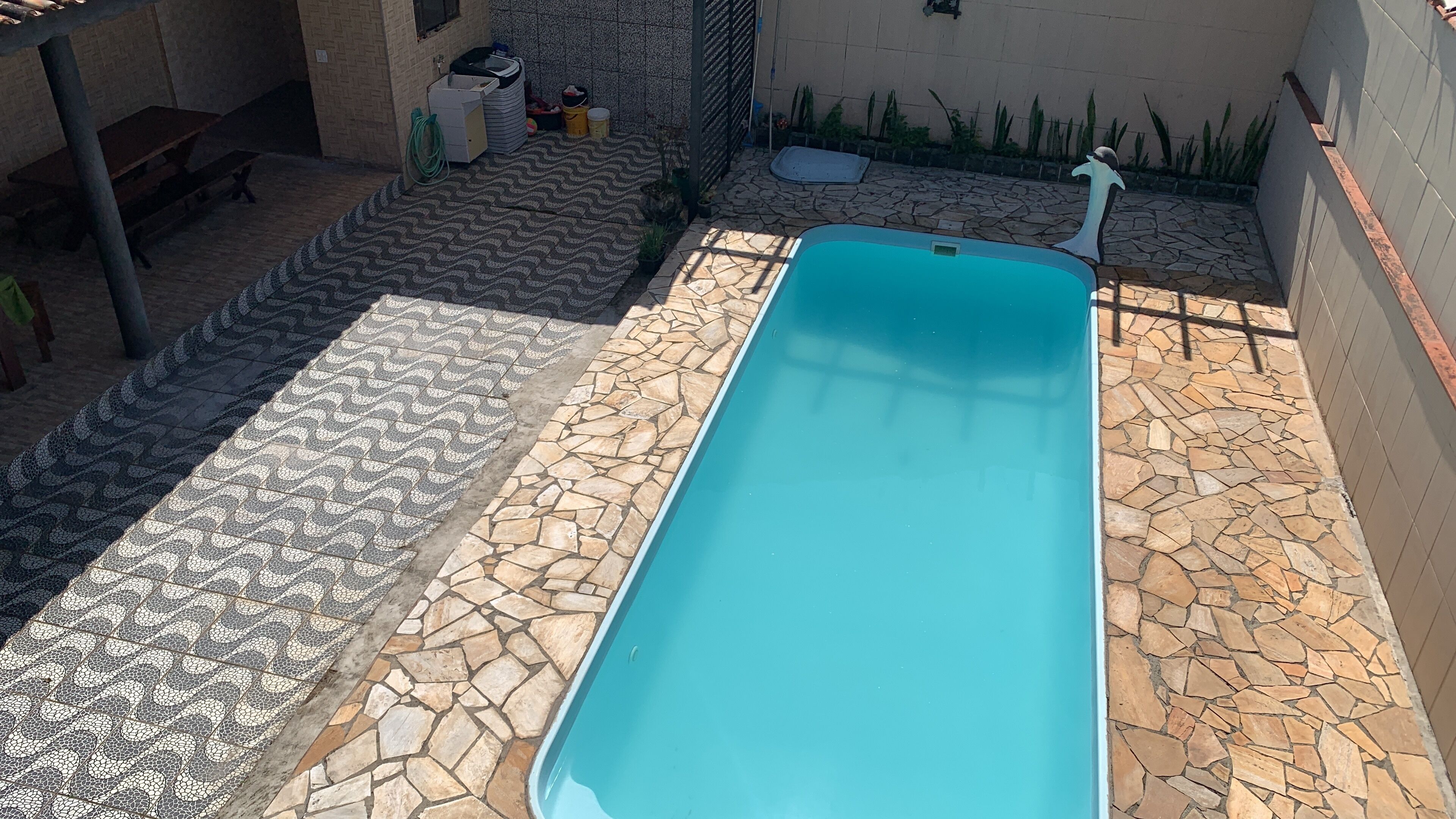 Ein Schwimmbecken mit gefliestem Beckenrand, umgeben von einer Steinmauer und einer kleinen Gartenanlage mit Pflanzen.