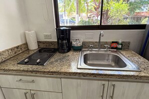 A kitchen with a stove, coffee maker, sink, and window view. - Walk to Beach! Studio w/ Pool Access at Club Voca (Playas del Coco)