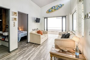 A modern living room with a sofa, a coffee table, and a television. There is a large window providing a view outside. - Pool & Entertaining Patio: Playa Carrillo Home (Playa Carrillo)