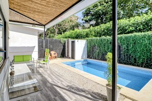 A modern outdoor pool area with a glass enclosure, a seating area with chairs, and a view of a hedge and trees. - Pool & Entertaining Patio: Playa Carrillo Home (Playa Carrillo)