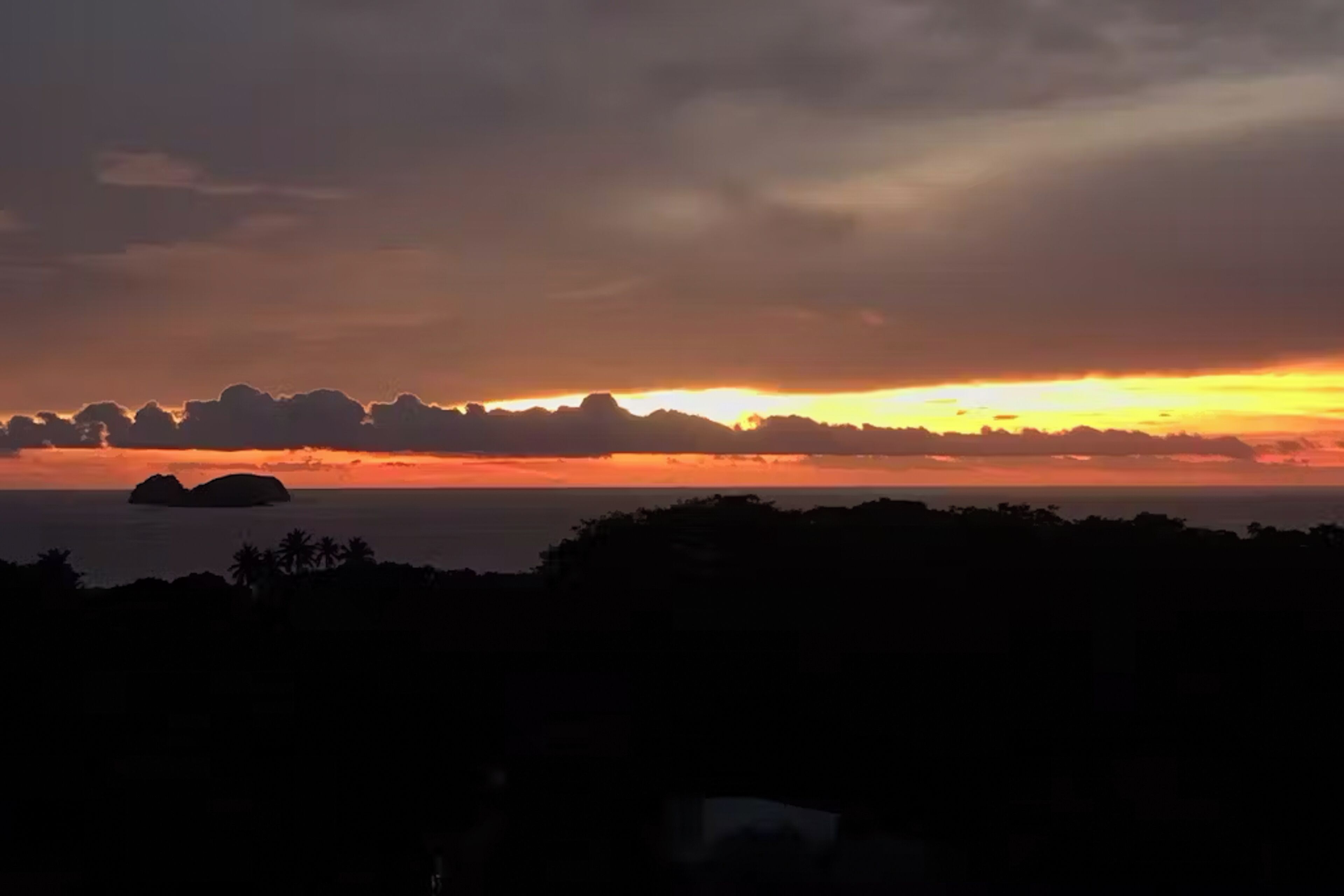 Un coucher de soleil sur la côte, avec les silhouettes de la terre ferme et d’une petite île.