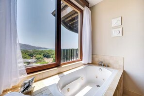A bathroom with a large bathtub, a window with curtains, and a view of a landscape. - Playa Hermosa Penthouse: Ocean Views, 2 Pools (Playa Hermosa)