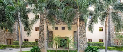 A hotel with a pool surrounded by palm trees and a stone facade.