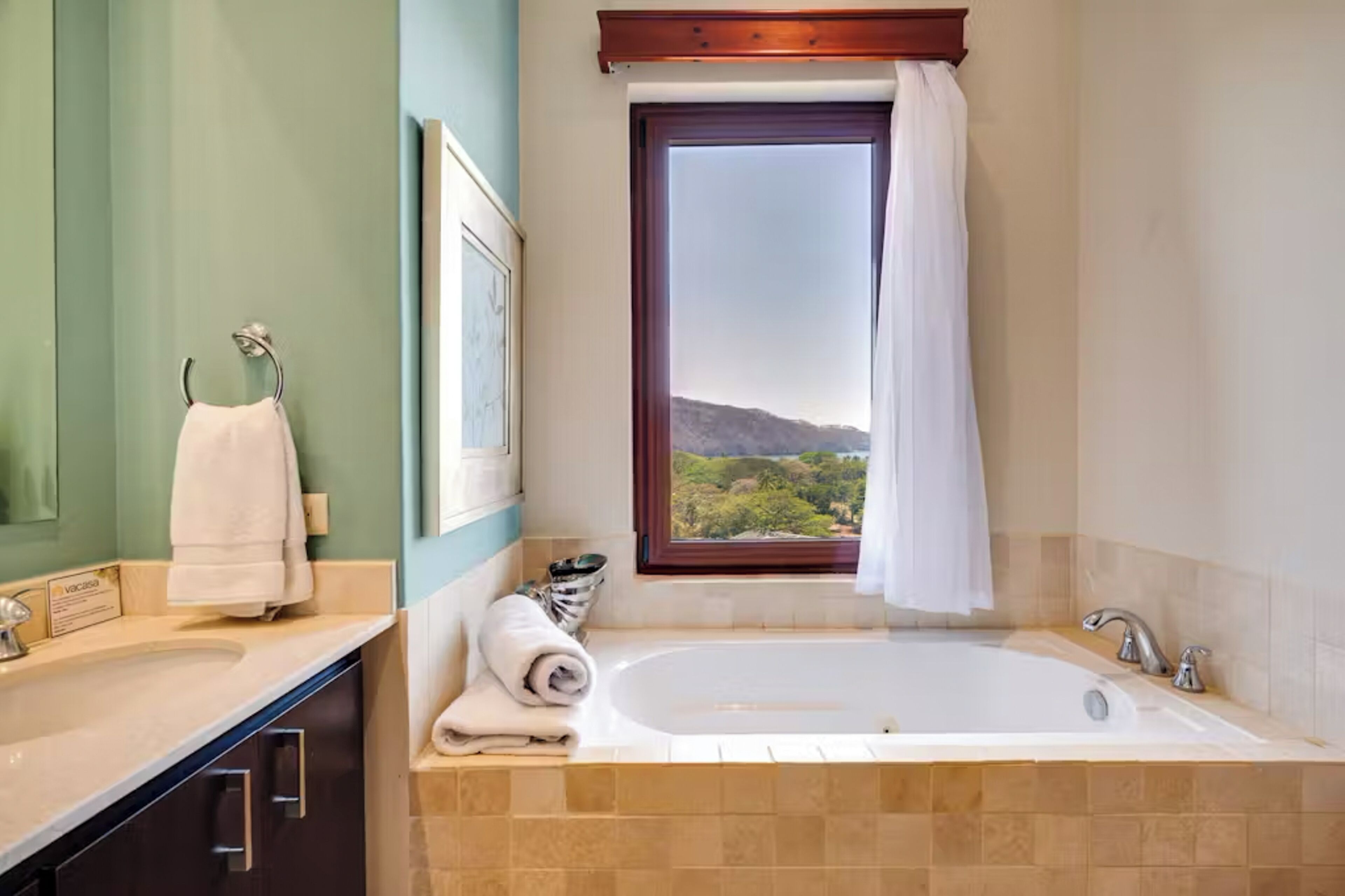 A bathroom with a bathtub, a sink, and a window offering a view of greenery.