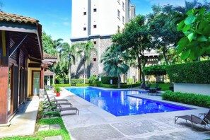A swimming pool with lounge chairs, a building with a tiled roof, and a tall structure in the background. - Playa Hermosa Penthouse: Ocean Views, 2 Pools (Playa Hermosa)