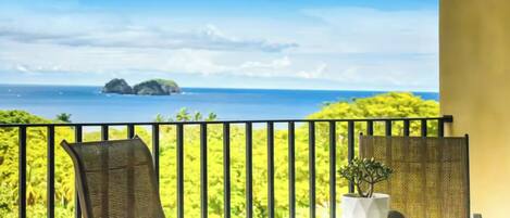 A balcony with a view of the sea and islands, a table with a plant, and a chair.