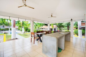 A covered outdoor dining area with a central concrete bar, ceiling fans, and a view of a pool and greenery. - 3-Unit Bundle: Club Voca Pool Access, Near Beach! (Playas del Coco)