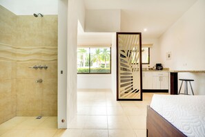 Ein modernes Badezimmer mit Dusche, einem Bett und Blick auf eine tropische Außenanlage.