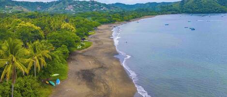 A beach with a clear view of the ocean and a forested hillside in the background.