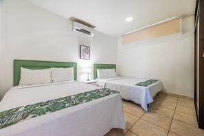 A hotel room with two beds, each with a green headboard and white bedding. There is a single bedside table with a lamp, and a ceiling-mounted air conditioning unit. - Playas del Coco Condo w/ Pool: Walk to Beach! (Playas del Coco)