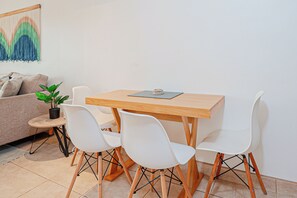 A small dining area with a wooden table and four white chairs, a potted plant, and a sofa with cushions. - 3 Mi to Beach: Modern Santa Cruz 2BR Condo (Tamarindo)
