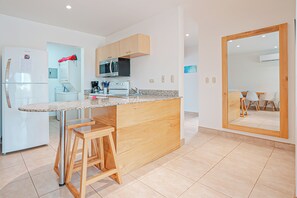 A modern kitchen with a granite countertop, wooden stools, and stainless steel appliances. - 3 Mi to Beach: Modern Santa Cruz 2BR Condo (Tamarindo)