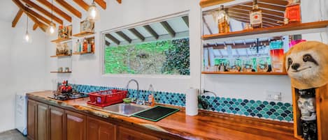 Cozinha com armários de madeira, pia vermelha e janela com vista para o verde.